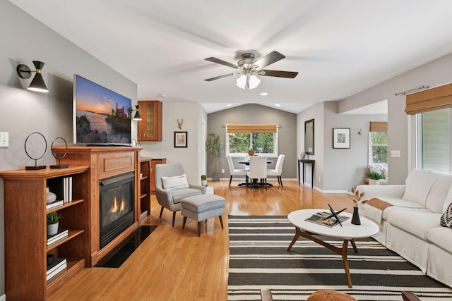living area featuring light wood-style floors, ceiling fan, vaulted ceiling, a glass covered fireplace, and recessed lighting