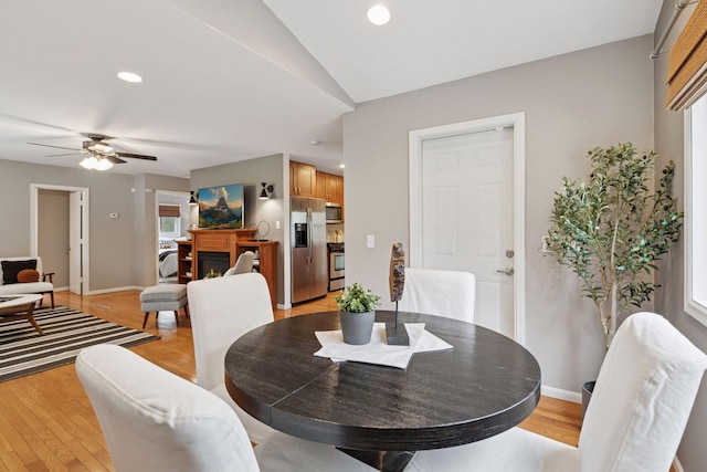 dining area with a warm lit fireplace, ceiling fan, baseboards, and light wood finished floors