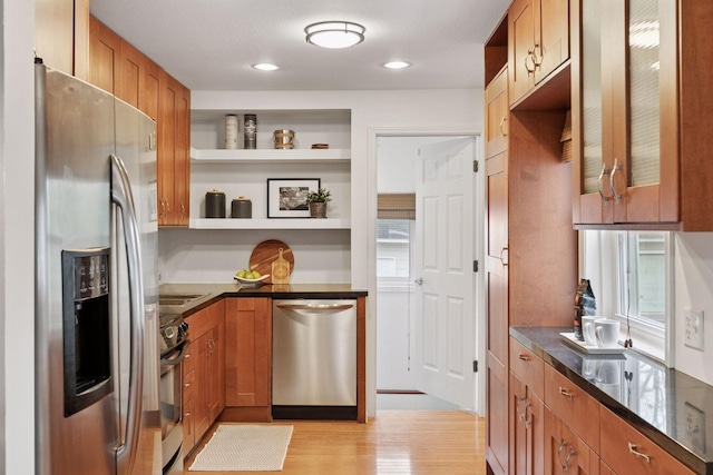 kitchen featuring brown cabinetry, open shelves, light wood-type flooring, dark stone counters, and stainless steel appliances