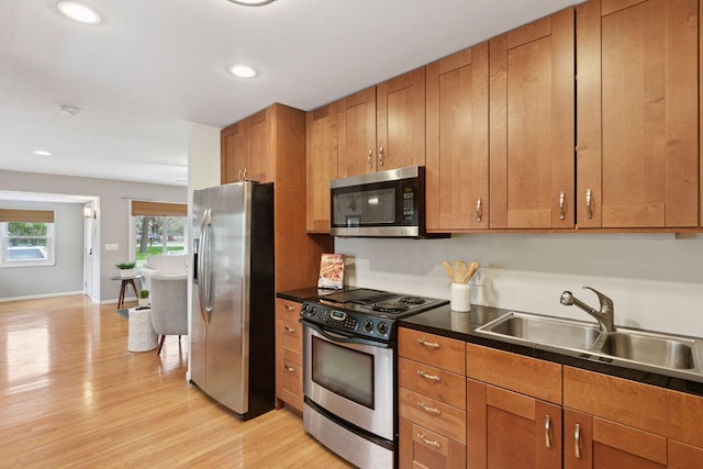 kitchen featuring brown cabinets, dark countertops, a sink, light wood-style flooring, and stainless steel appliances