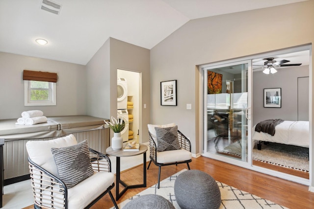 living area with light wood finished floors, lofted ceiling, stacked washer and dryer, and visible vents
