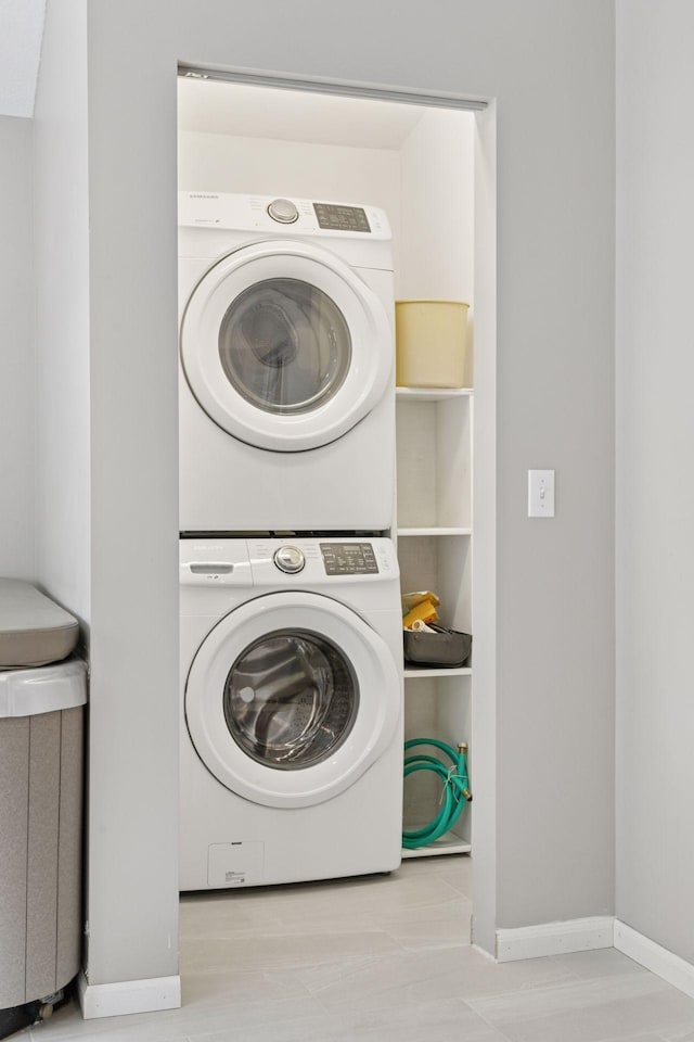 clothes washing area with baseboards, laundry area, and stacked washer / dryer
