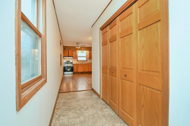corridor with baseboards, a sink, a textured ceiling, and stone finish floor