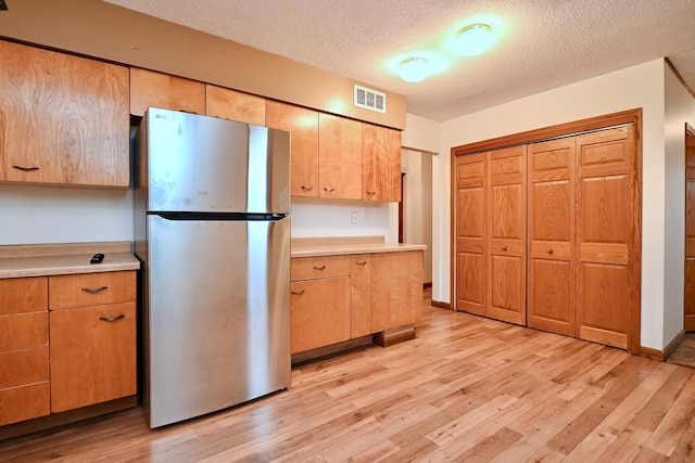 kitchen featuring visible vents, freestanding refrigerator, light wood-style floors, light countertops, and a textured ceiling