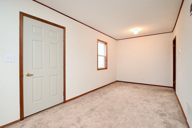 empty room featuring light colored carpet, ornamental molding, and baseboards