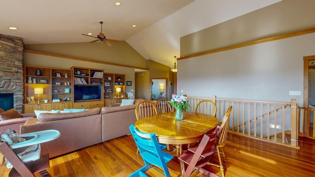 dining area featuring ceiling fan, wood finished floors, vaulted ceiling, and a fireplace