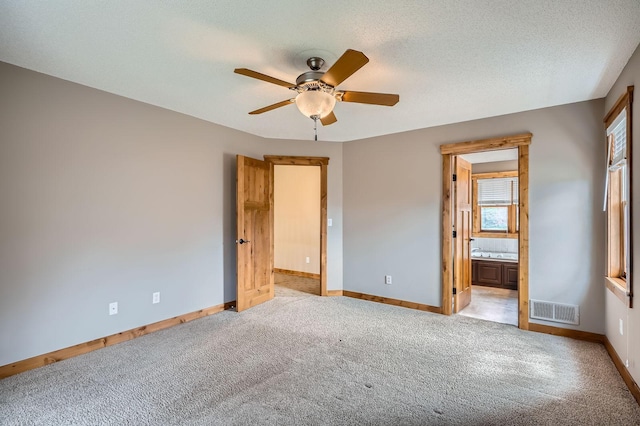 unfurnished bedroom featuring visible vents, baseboards, light colored carpet, a ceiling fan, and ensuite bath