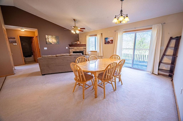 dining room with a stone fireplace, ceiling fan with notable chandelier, vaulted ceiling, and light carpet