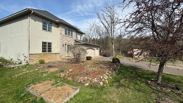 view of property exterior with stone siding, a garage, a vegetable garden, a lawn, and driveway