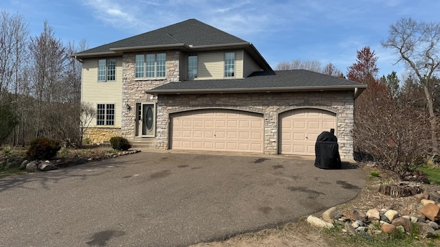 view of front of property featuring an attached garage, a shingled roof, stone siding, and aphalt driveway