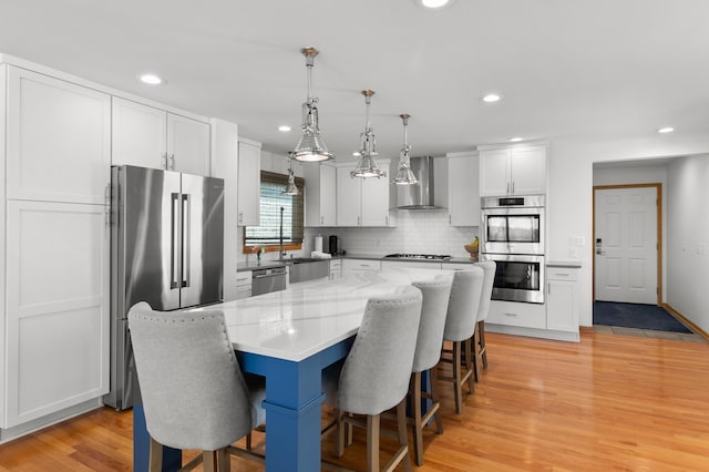 kitchen with appliances with stainless steel finishes, wall chimney range hood, a breakfast bar area, light wood-type flooring, and tasteful backsplash