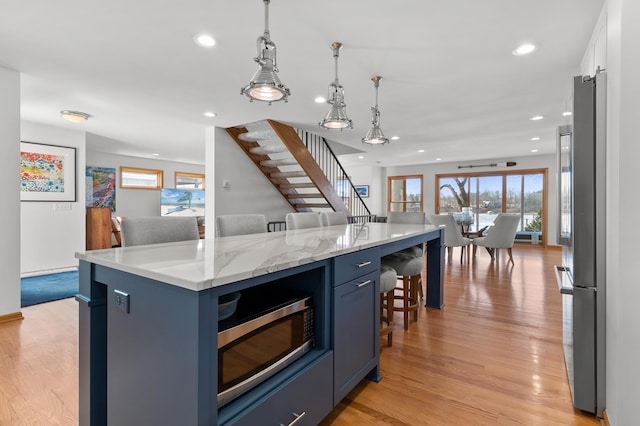kitchen featuring appliances with stainless steel finishes, blue cabinetry, a breakfast bar area, light wood-style floors, and recessed lighting