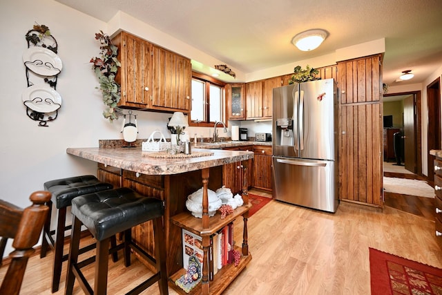 kitchen with brown cabinetry, open shelves, light wood-type flooring, a peninsula, and stainless steel fridge