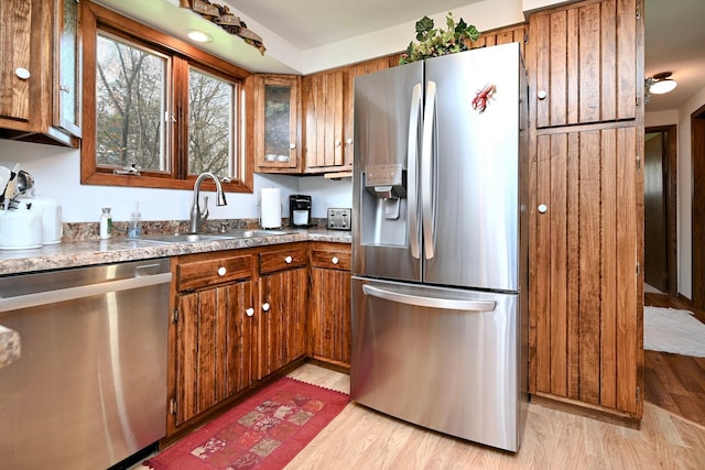kitchen featuring stainless steel appliances, brown cabinetry, a sink, and light wood-style floors