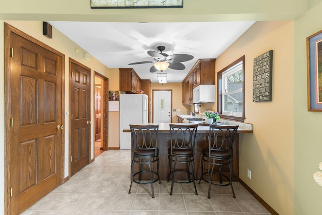10851 Olive St NW, Coon Rapids, MN 55448 - kitchen featuring white appliances, a peninsula, a kitchen bar, baseboards, and ceiling fan