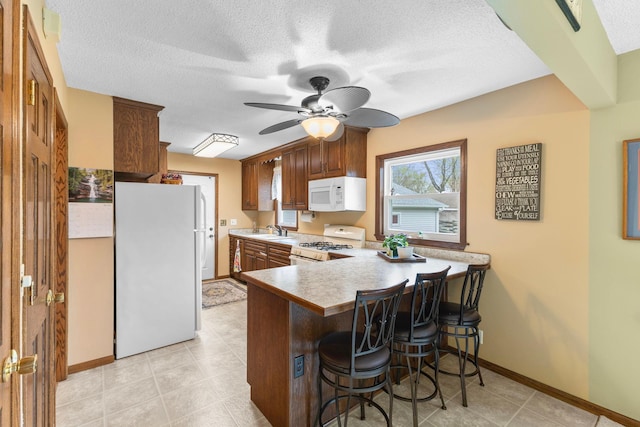 10851 Olive St NW, Coon Rapids, MN 55448 - kitchen featuring white appliances, a peninsula, a sink, a kitchen breakfast bar, and light countertops