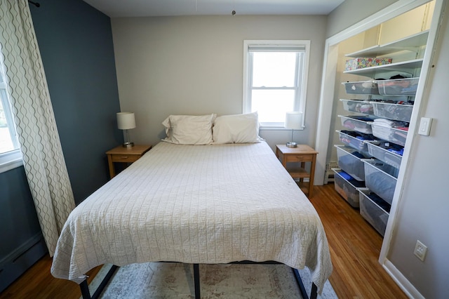 bedroom featuring a baseboard heating unit, wood finished floors, and a closet