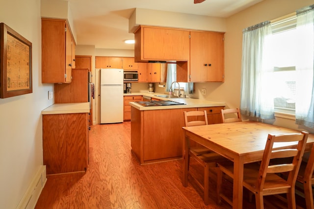 kitchen featuring freestanding refrigerator, a peninsula, light wood-type flooring, stainless steel microwave, and a sink