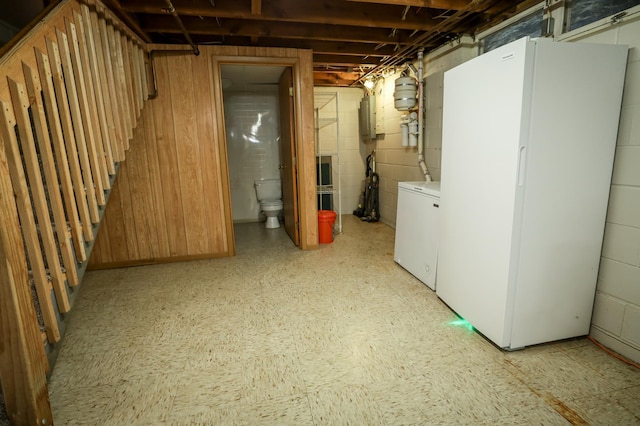 unfinished below grade area with freestanding refrigerator, washer and dryer, light floors, electric panel, and concrete block wall