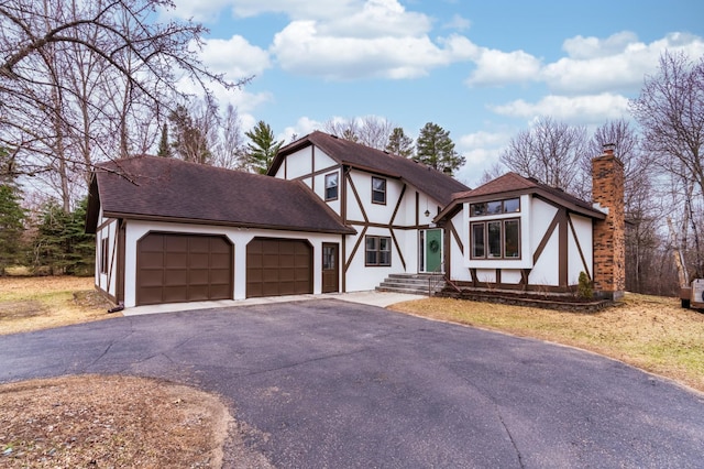 tudor home featuring a garage, stucco siding, driveway, and a chimney