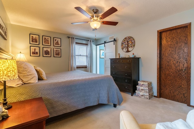 carpeted bedroom featuring ceiling fan, visible vents, and a barn door