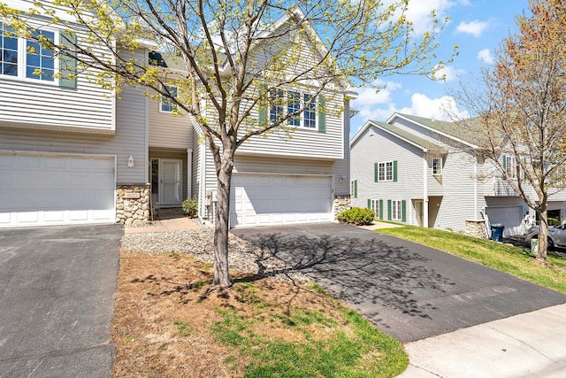 townhome / multi-family property featuring stone siding, an attached garage, and driveway