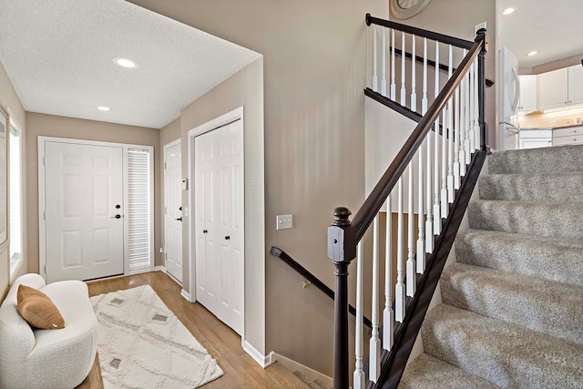 entrance foyer with light wood-type flooring, baseboards, recessed lighting, and a textured ceiling