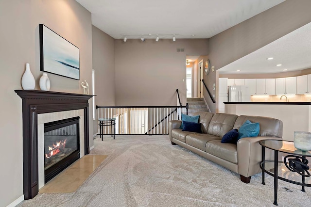 carpeted living area featuring rail lighting, a tiled fireplace, recessed lighting, and stairs
