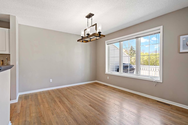 unfurnished dining area with light wood-type flooring, a chandelier, baseboards, and a textured ceiling