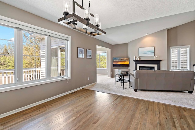 living room with baseboards, a chandelier, lofted ceiling, wood finished floors, and a glass covered fireplace