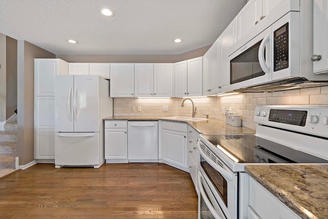 kitchen with white appliances, a sink, white cabinetry, a textured ceiling, and dark wood finished floors