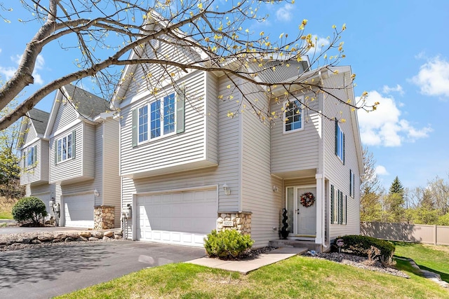 traditional-style house featuring fence, stone siding, an attached garage, and asphalt driveway