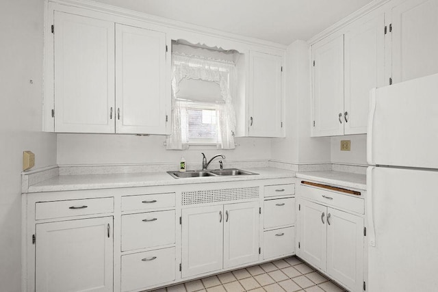 kitchen featuring freestanding refrigerator, light countertops, white cabinetry, and a sink