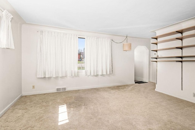 basement featuring arched walkways, baseboards, visible vents, and carpet