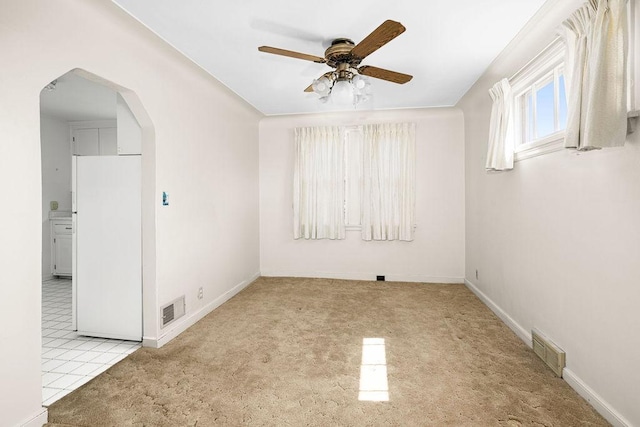 empty room with carpet, visible vents, a ceiling fan, and arched walkways