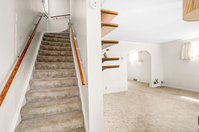 stairway with carpet, baseboards, and arched walkways