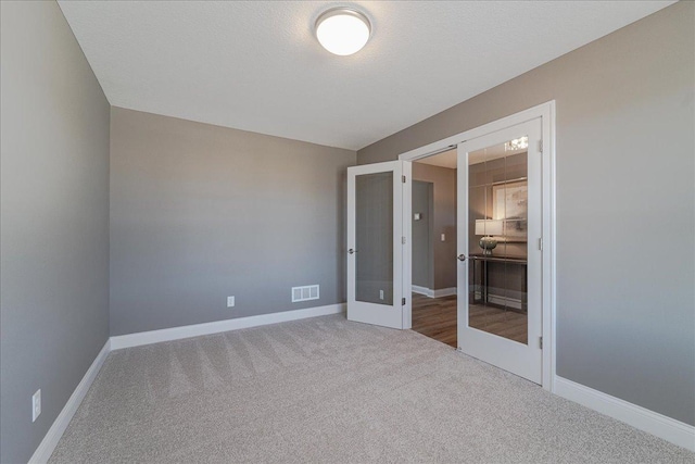 carpeted spare room featuring french doors, baseboards, and visible vents