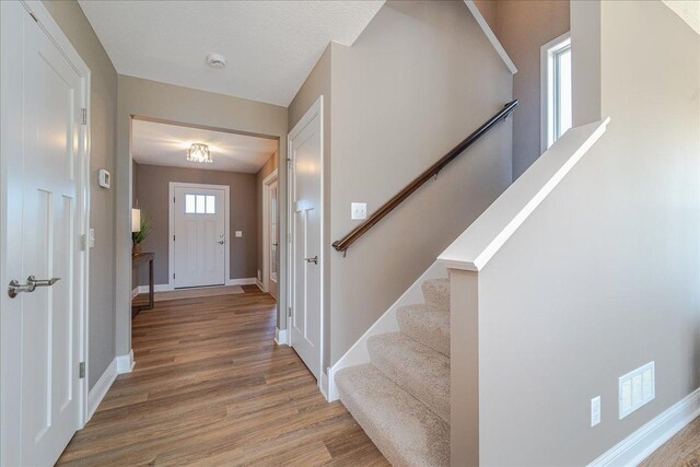 entryway featuring light wood-style floors, baseboards, stairway, and visible vents