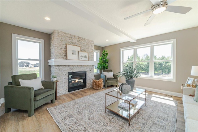 living room featuring visible vents, baseboards, a stone fireplace, ceiling fan, and light wood-type flooring