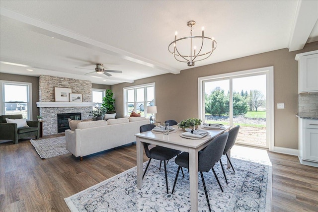 dining room featuring dark wood-type flooring, ceiling fan with notable chandelier, beam ceiling, and a fireplace