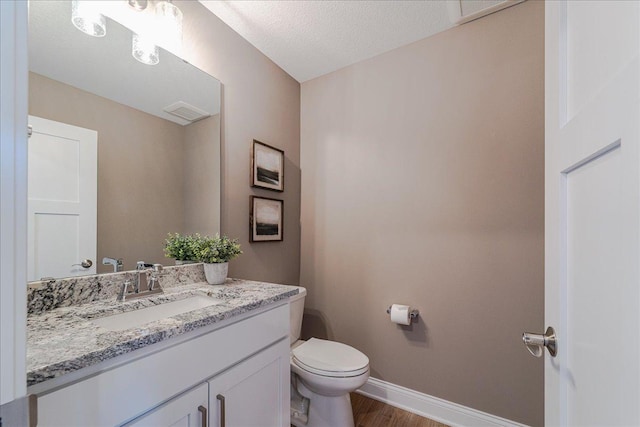 half bath with a textured ceiling, wood finished floors, baseboards, vanity, and toilet