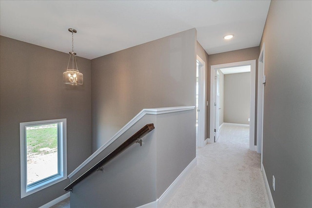 hall featuring baseboards, light colored carpet, a chandelier, and an upstairs landing