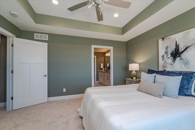 carpeted bedroom with baseboards, visible vents, a tray ceiling, and ensuite bath