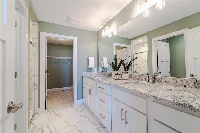 bathroom with double vanity, marble finish floor, a spacious closet, a sink, and a stall shower