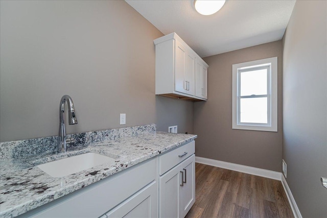 washroom with cabinet space, a sink, hookup for a washing machine, baseboards, and dark wood-style floors