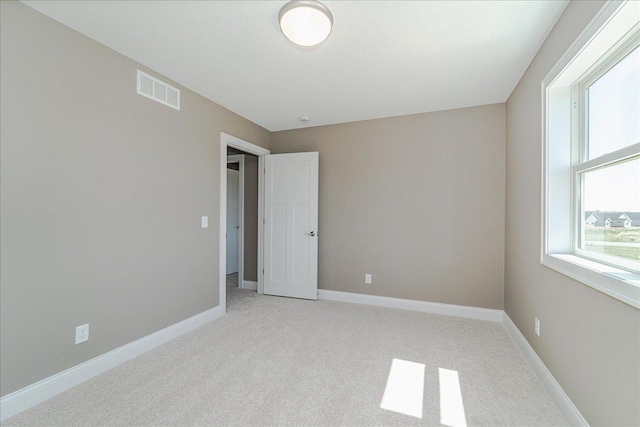 unfurnished room with light colored carpet, baseboards, visible vents, and a wealth of natural light