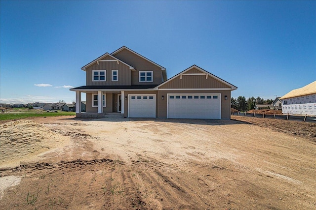 craftsman-style home with a porch, dirt driveway, and an attached garage