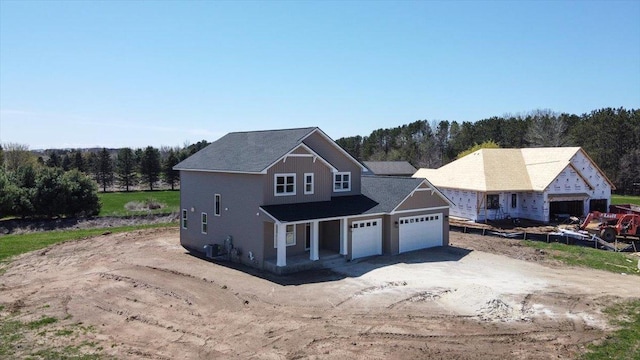 view of front of home with an attached garage, central AC, a porch, a view of trees, and driveway