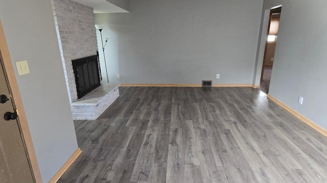 unfurnished living room with visible vents, baseboards, a brick fireplace, and wood finished floors