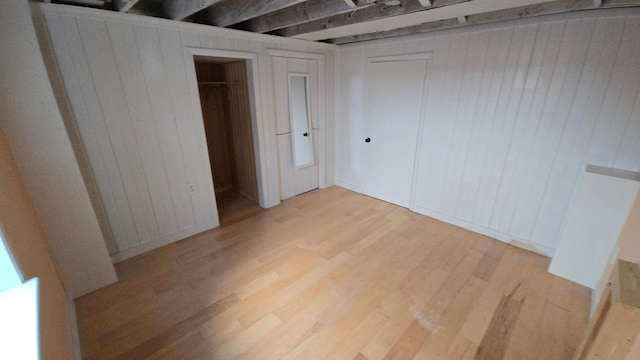 unfurnished bedroom with light wood-type flooring, wood walls, and multiple closets